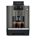 A modern automatic espresso machine in dark gray and black, shown from the front with two cups of espresso filled under the dispensing area on a white background.