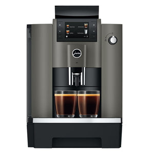A modern automatic espresso machine in dark gray and black, shown from the front with two cups of espresso filled under the dispensing area on a white background.