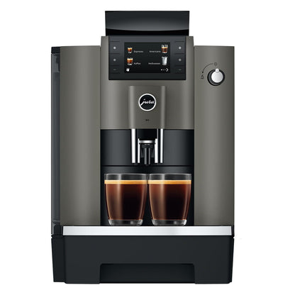 A modern automatic espresso machine in dark gray and black, shown from the front with two cups of espresso filled under the dispensing area on a white background.